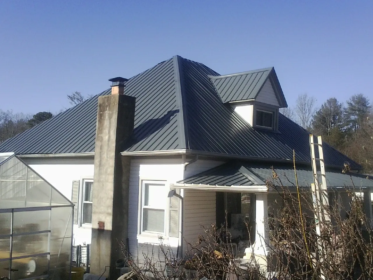 Dark blue standing seam metal roof on a white farmhouse with dormer — Slate & Tile Roof Repair by Roofing Brothers in Hawley