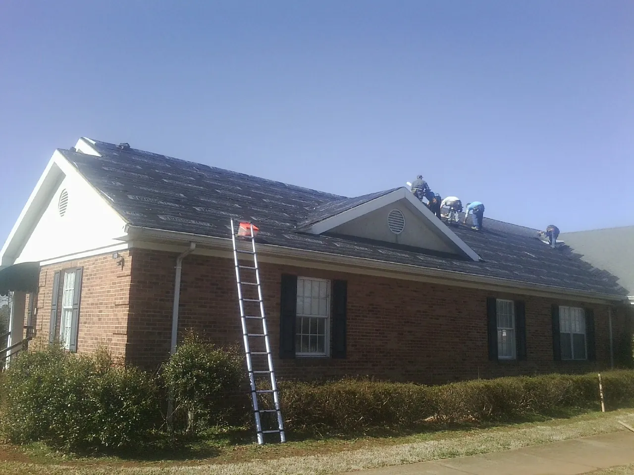 Crew tearing shingles off a brick ranch roof with a ladder set — Metal Roof Repair work by our crew in Hawley