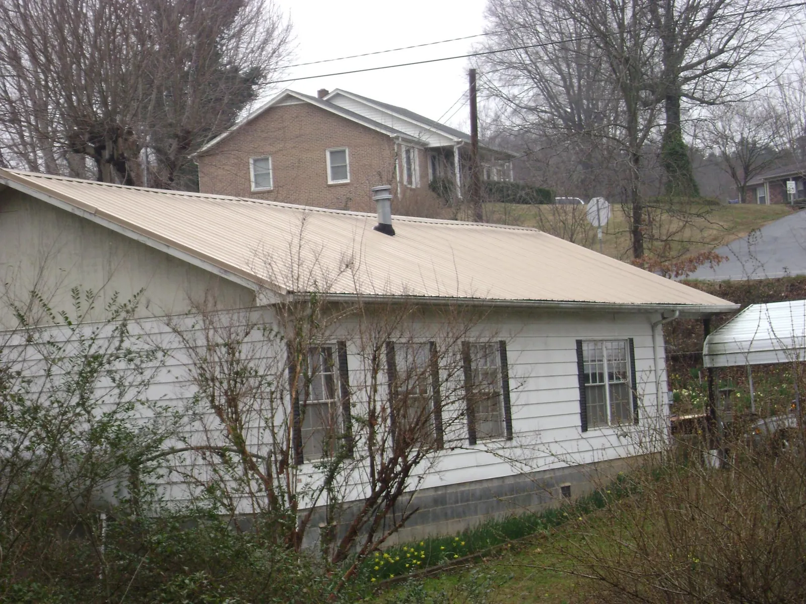 Tan metal roof on a white sided house set into a hillside — Commercial Roofing by Roofing Brothers in Hawley
