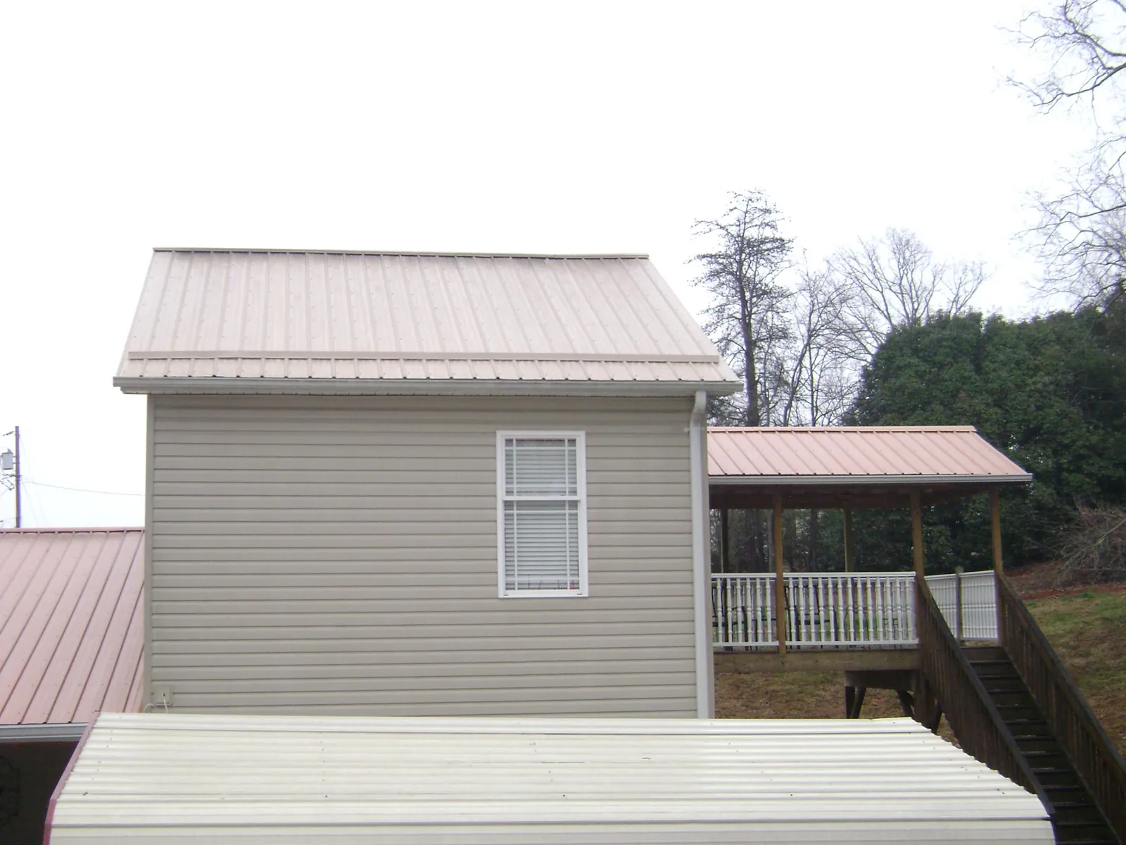 Tan metal roofs on a two story addition and attached porch, from a Roof Replacement job in Hawley